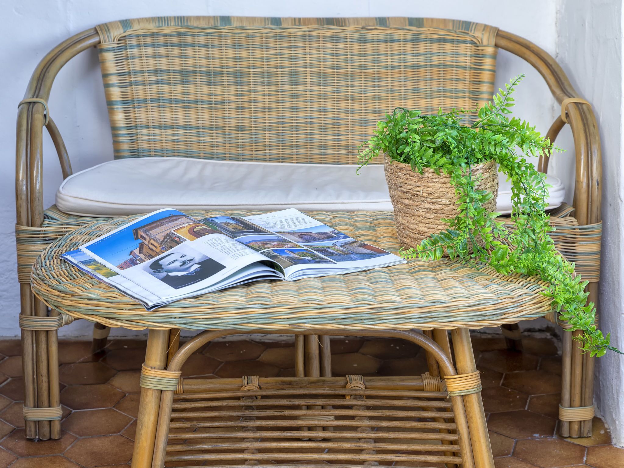 A wicker sofa with a woven seat and backrest, a woven basket with a plant, and a magazine on the seat.