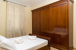 Un dormitorio con una cama, un armario de madera y una ventana con cortinas traslúcidas.