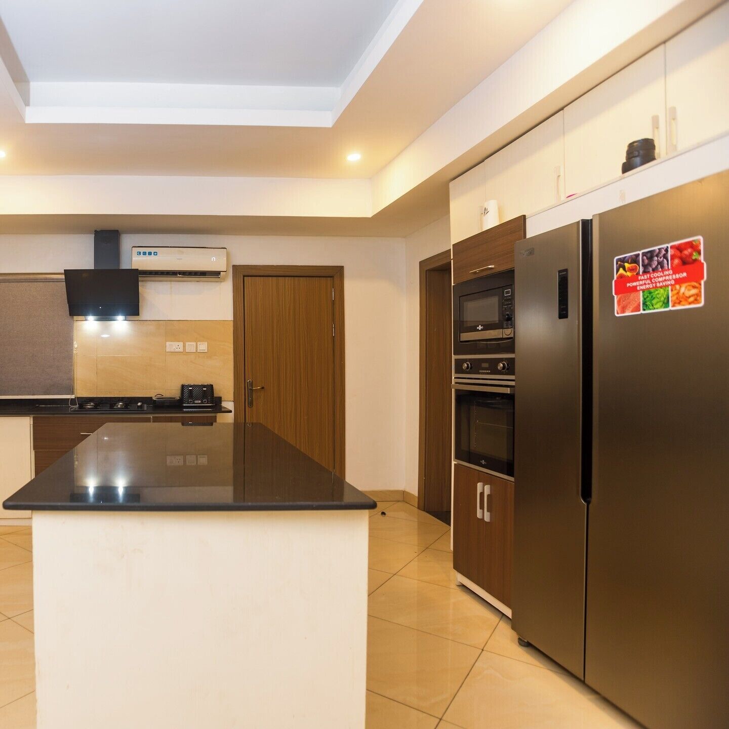Una cocina moderna con una isla central, horno empotrado y un refrigerador con una etiqueta.