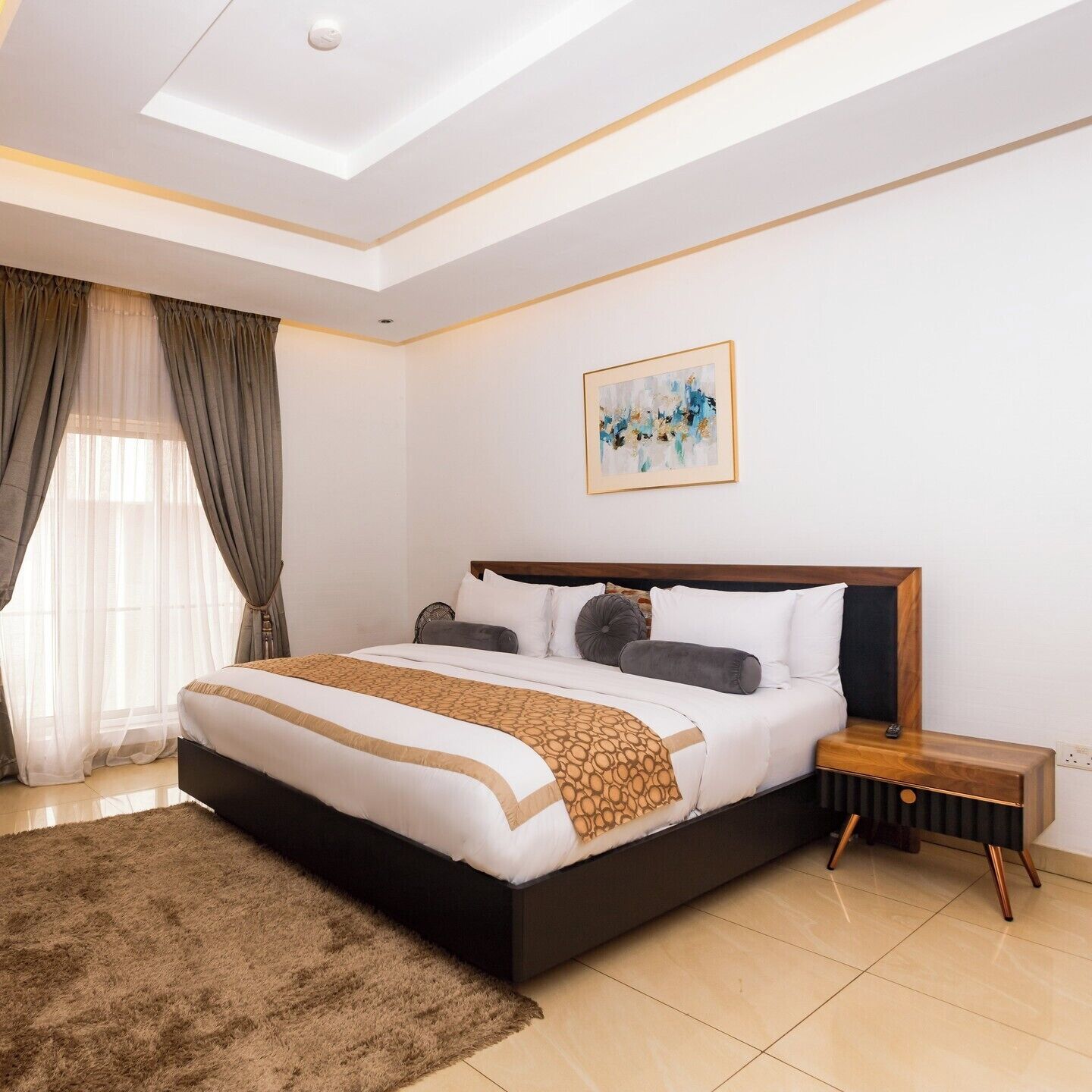 A modern bedroom with a large bed, a bedside table, a ceiling light, and a painting on the wall.