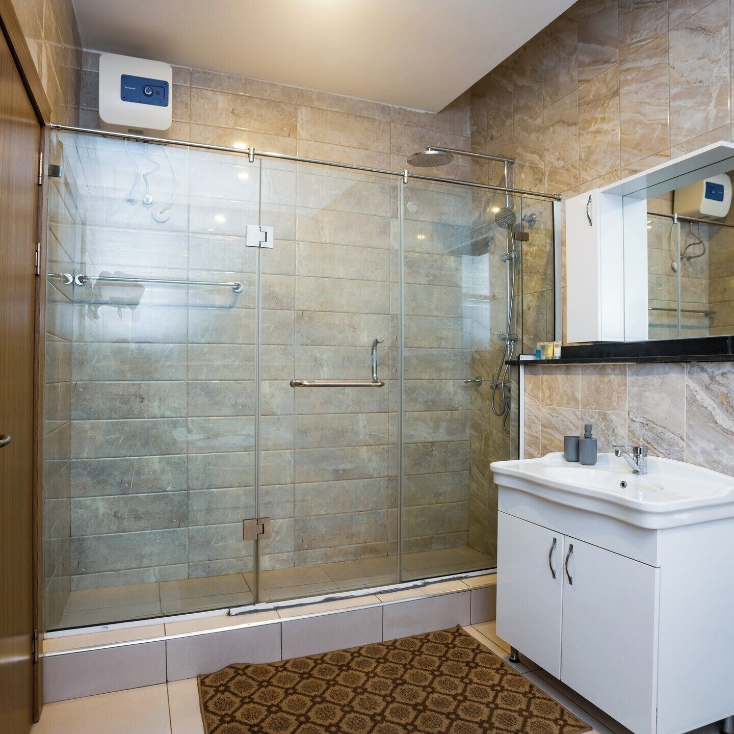 Une salle de bain moderne avec une douche à parois de verre, un lavabo blanc avec un miroir au-dessus, et un tapis à motifs sur le sol.