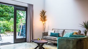 Una sala de estar moderna con un sofá gris, un sillón verde azulado y una alfombra estampada. También se ve una lámpara de pie alta y una planta en maceta.
