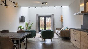 Una cocina moderna con estufa integrada, un comedor con mesa y sillas de madera, y un amplio ventanal corredero que da a un jardín.