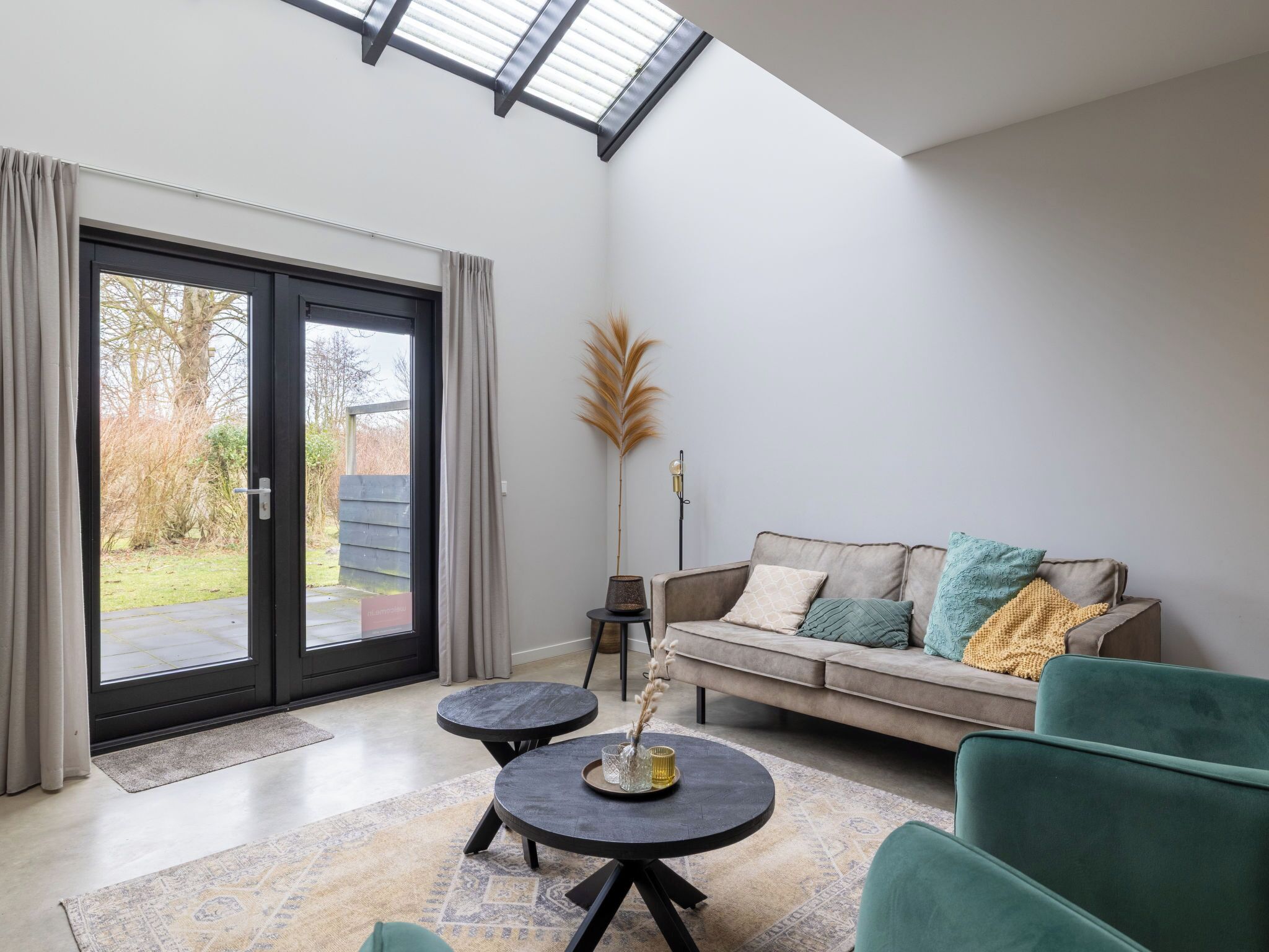 Uma sala de estar moderna com um sofá, duas mesinhas e uma grande porta de vidro deslizante que dá para um jardim.