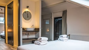 Habitación de hotel con cama, espejo redondo, lavabo y ventana con cortinas.