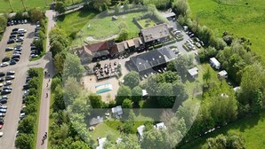 Vista aérea de una propiedad con un amplio estacionamiento, piscina y varios edificios que combinan arquitectura moderna y tradicional.