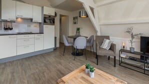 A modern kitchen with white cabinets, a dining area with a round table and chairs, a cozy seating area with a sofa and a TV stand, and a wooden floor. - StrandLust Westkapelle by Interhome (Westkapelle)