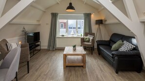 A cozy loft-style living room with a wooden coffee table, a black leather sofa, and a television on a stand. - StrandLust Westkapelle by Interhome (Westkapelle)