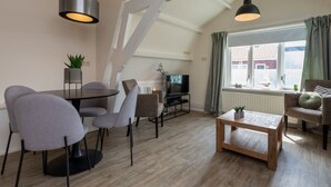 A modern living room with a dining area, wooden flooring, and a large window with curtains. - StrandLust Westkapelle by Interhome (Westkapelle)