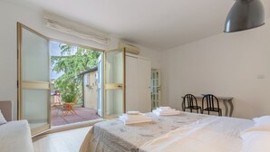 Quarto com cama, escrivaninha, cadeiras, porta de vidro deslizante para área externa e guarda-roupa.