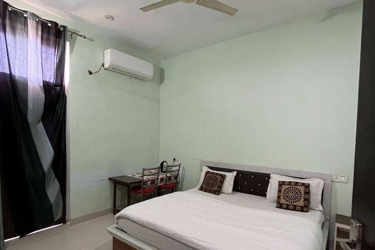 A bedroom with a bed, a desk, a chair, a ceiling fan, and an air conditioning unit.