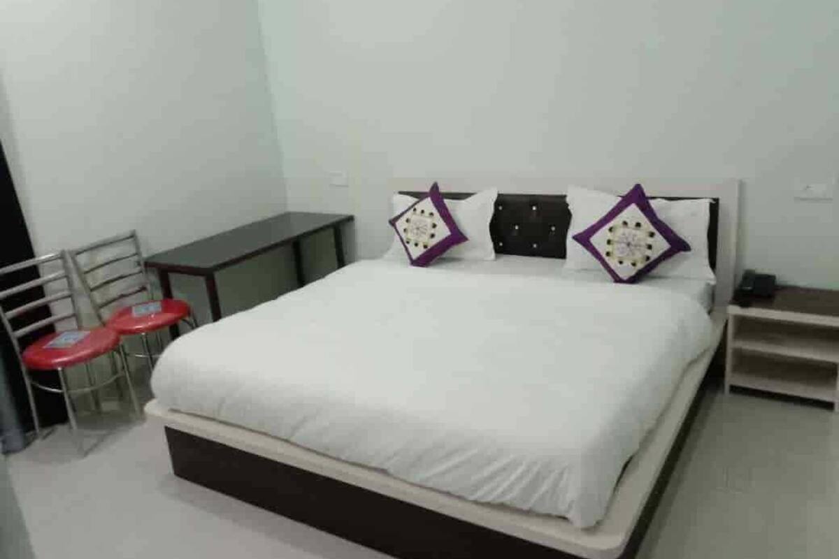 A bedroom with a bed, two red chairs, a small table, and a white wall.
