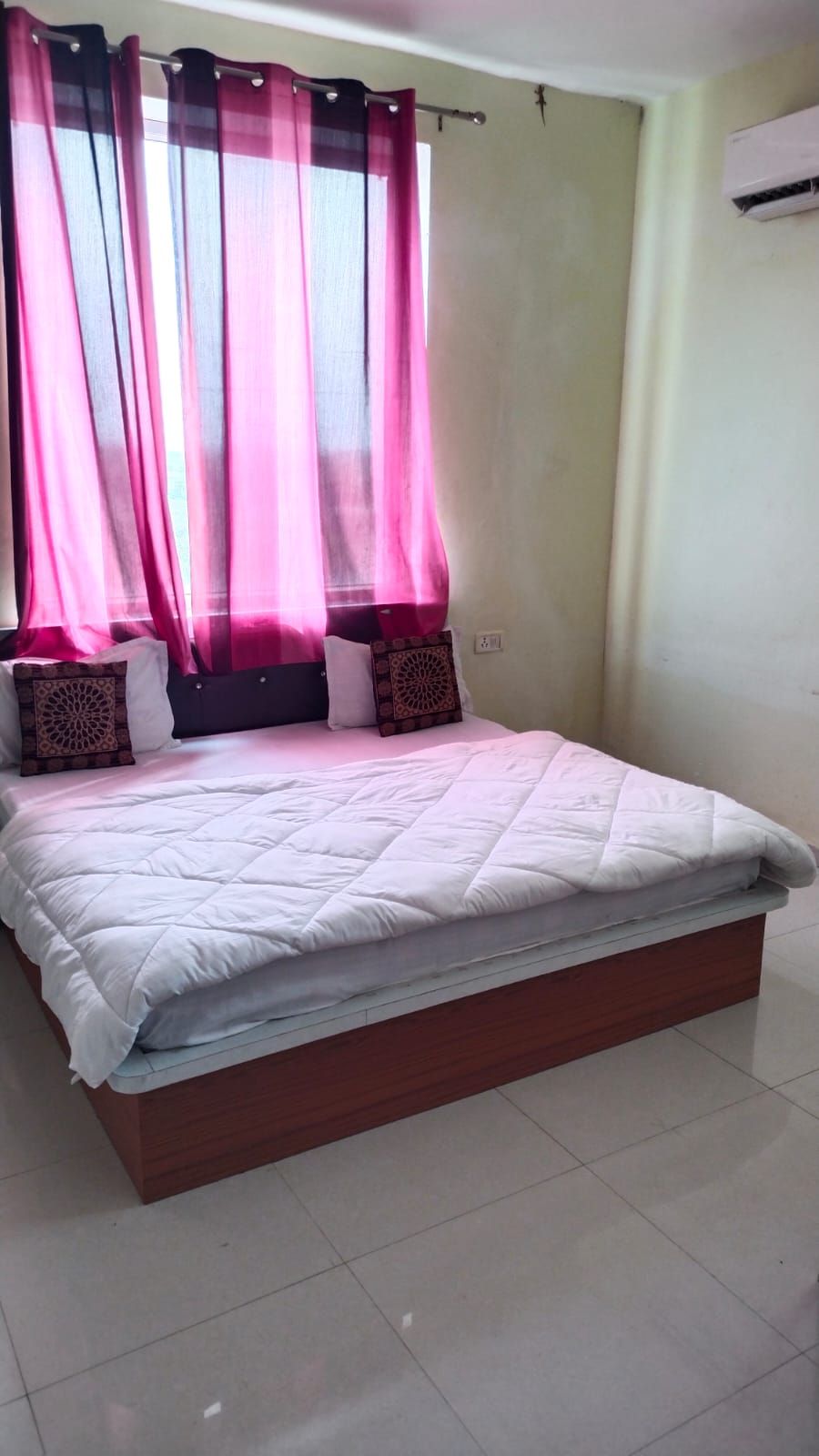 Un dormitorio con cama, cortinas y un equipo de aire acondicionado.