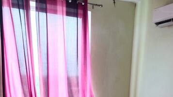 Un dormitorio con cama, cortinas y un equipo de aire acondicionado.