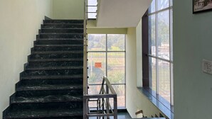 Eine Treppe mit Metallgeländer, einer Zwischenebene und Blick durch große Fenster nach draußen.