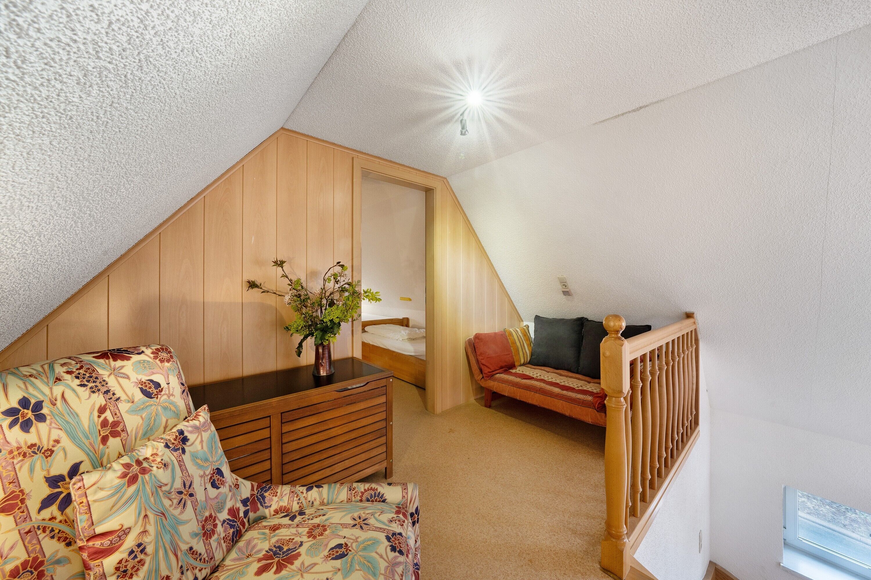 A room with a sloped ceiling, a bed, a sofa, a dresser, and a staircase.