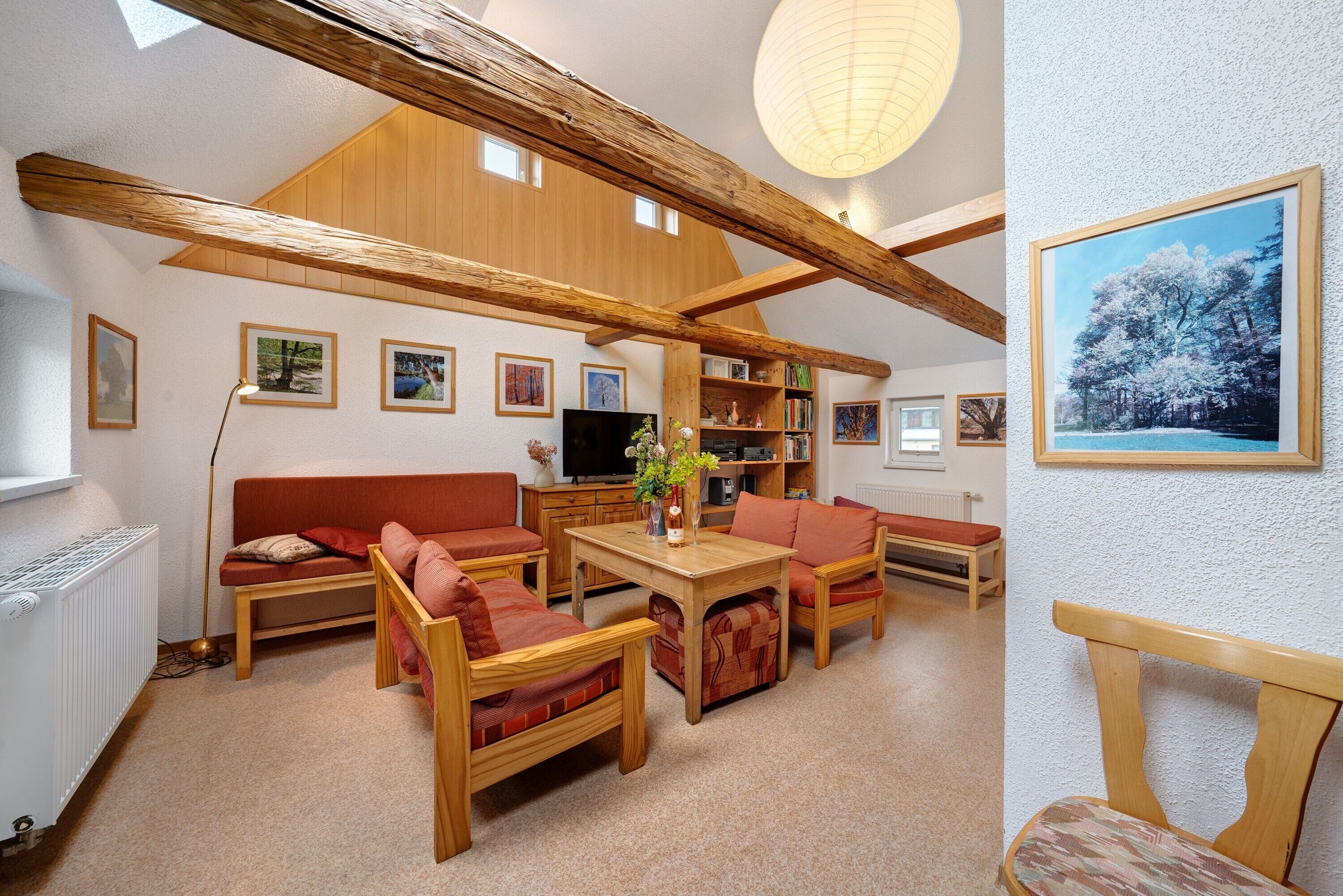 Ein gemütliches Wohnzimmer mit Holzbalkendecke, einem Fernseher und einem Bücherregal.