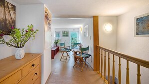 Un couloir avec une commode en bois, un coin repas avec des chaises et un escalier avec une rampe en bois.