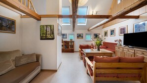 Un vaste espace de vie doté d’un plafond haut, de poutres en bois, d’un canapé, d’une table à manger et d’un téléviseur.
