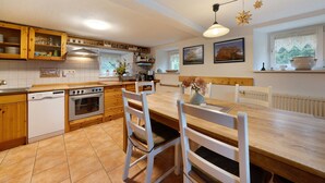 Une cuisine avec des meubles en bois, un lave-vaisselle, un four, une table à manger avec des chaises et une fenêtre donnant sur un paysage verdoyant.