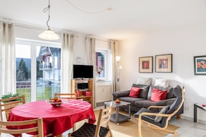 A living room with a dining table, sofa, TV, and artwork on the wall.