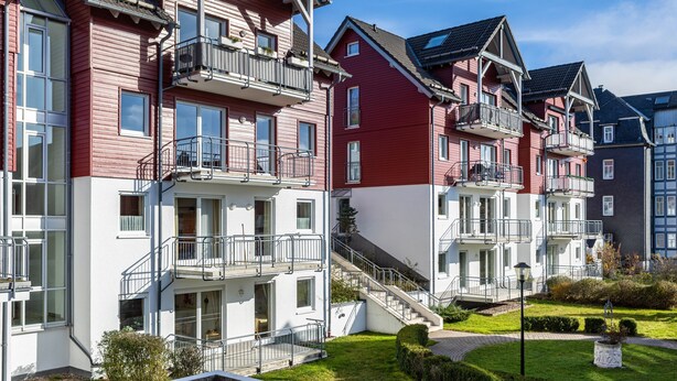 A row of modern multi-story residential buildings with balconies, a well-maintained lawn, and a clear sky. - Apartment 'Tannenblick 1-1' with Mountain View, Private Terrace and Wi-Fi (Oberhof)