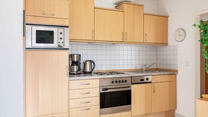 A kitchen with wooden cabinets, a built-in microwave, a stove, a sink, and a clock on the wall. - Apartment 'Tannenblick 1-1' with Mountain View, Private Terrace and Wi-Fi (Oberhof)