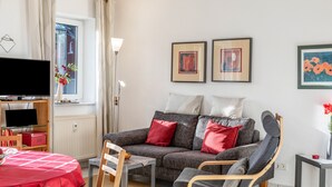 A living room with a sofa, armchair, TV, and artwork on the wall. - Apartment 'Tannenblick 1-1' with Mountain View, Private Terrace and Wi-Fi (Oberhof)