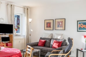 Un salon avec un canapé, un fauteuil, une télévision et des œuvres d’art accrochées au mur.