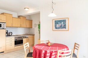 A kitchen with wooden cabinets, a microwave, an oven, and a dining table with a red tablecloth.