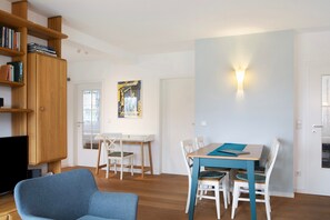 A modern living room with a blue sofa, wooden bookshelves, a dining table with chairs, and a wall-mounted light fixture. - Apartment 'Tannenblick 6-2' with Mountain View, Balcony and Wi-Fi (Oberhof)