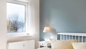 Makuuhuoneessa on sänky, yöpöytä lampun kanssa, ikkuna ja patteri.