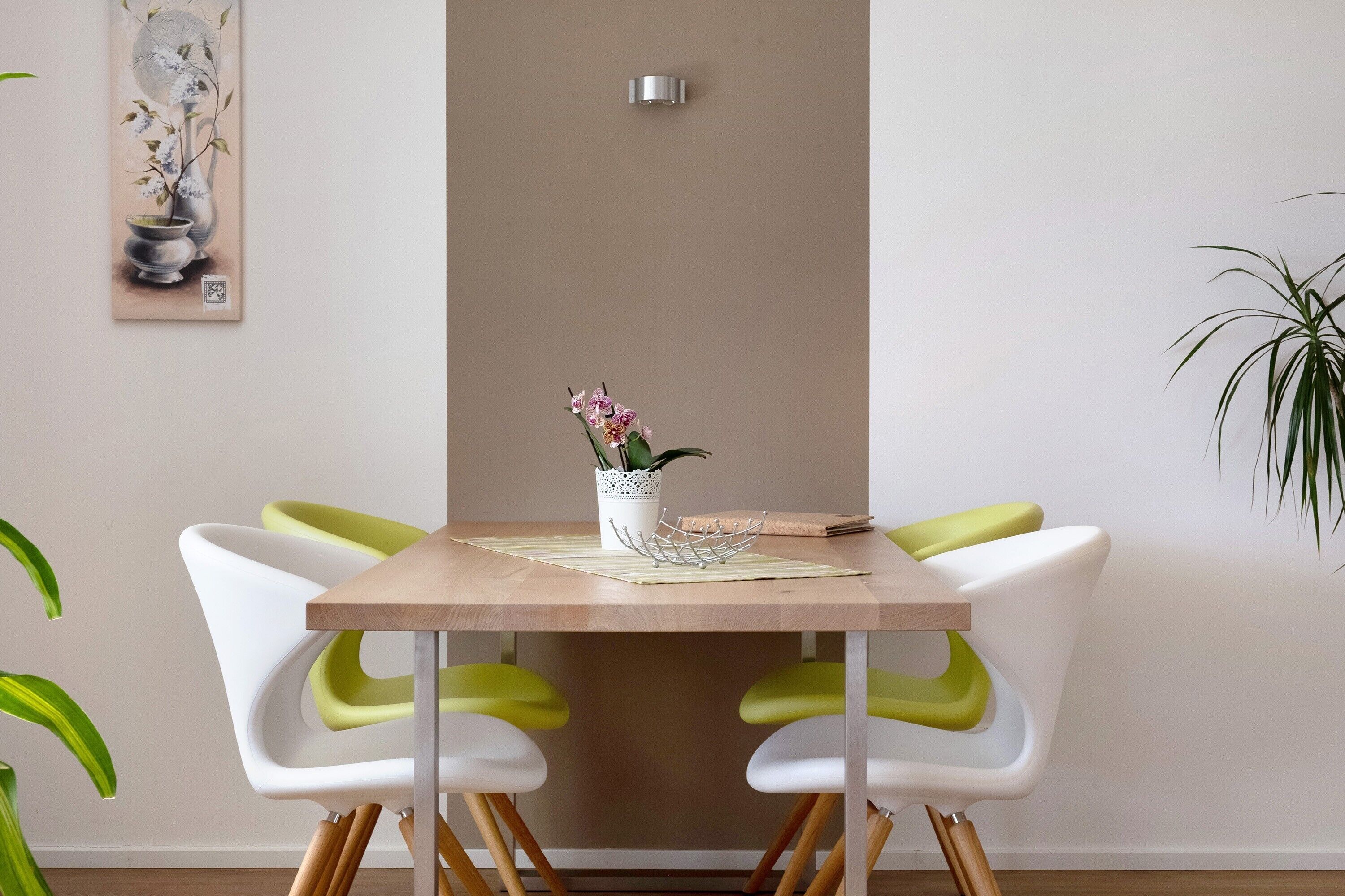 A dining table with two chairs, a vase with flowers, and a wall-mounted light fixture.