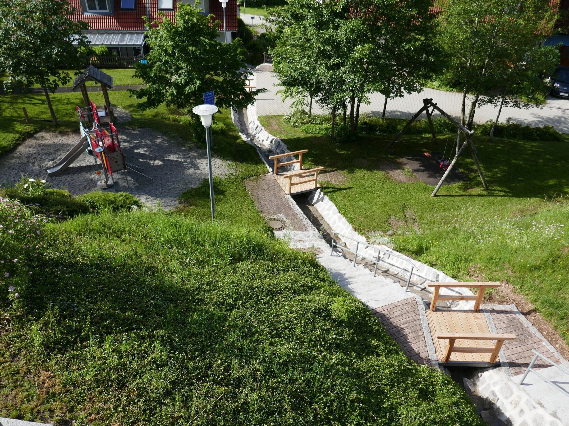 Um parque com parquinho, calçada pavimentada e banco de madeira.