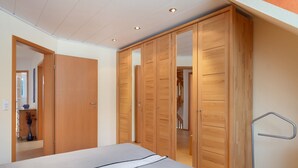 Een slaapkamer met een bed, een houten garderobe en een metalen kapstok.