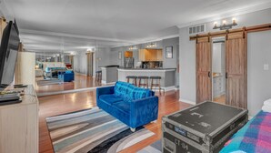 A spacious living area with a blue sofa, a wooden dining table, and a kitchen in the background. - Honky Tonk Angels Suite (Nashville)
