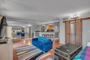 Un amplio salón con un sofá azul, una mesa de comedor de madera y una cocina al fondo.