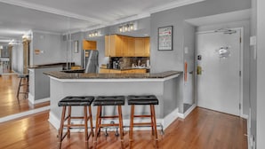 A modern kitchen with a central island, wooden bar stools, and a refrigerator. - Honky Tonk Angels Suite (Nashville)