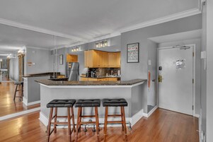 Una cocina moderna con una isla central, taburetes de bar de madera y un refrigerador.