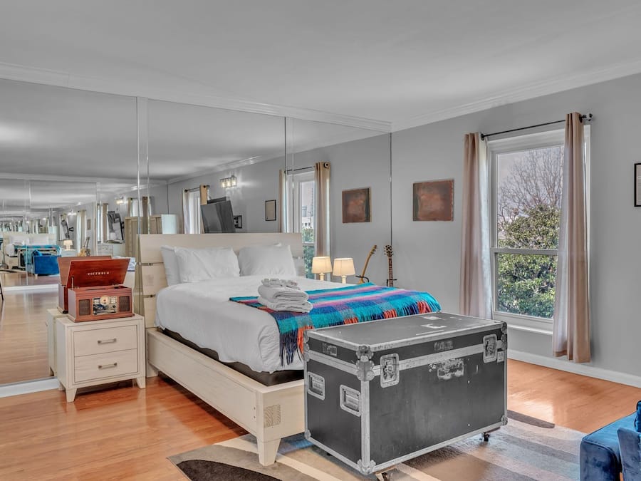 Quarto de hotel moderno com uma cama grande, mesas de cabeceira, uma mala e vista para o exterior.