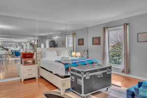 Una habitación de hotel moderna con una cama grande, mesitas de noche, una maleta y vistas al exterior.