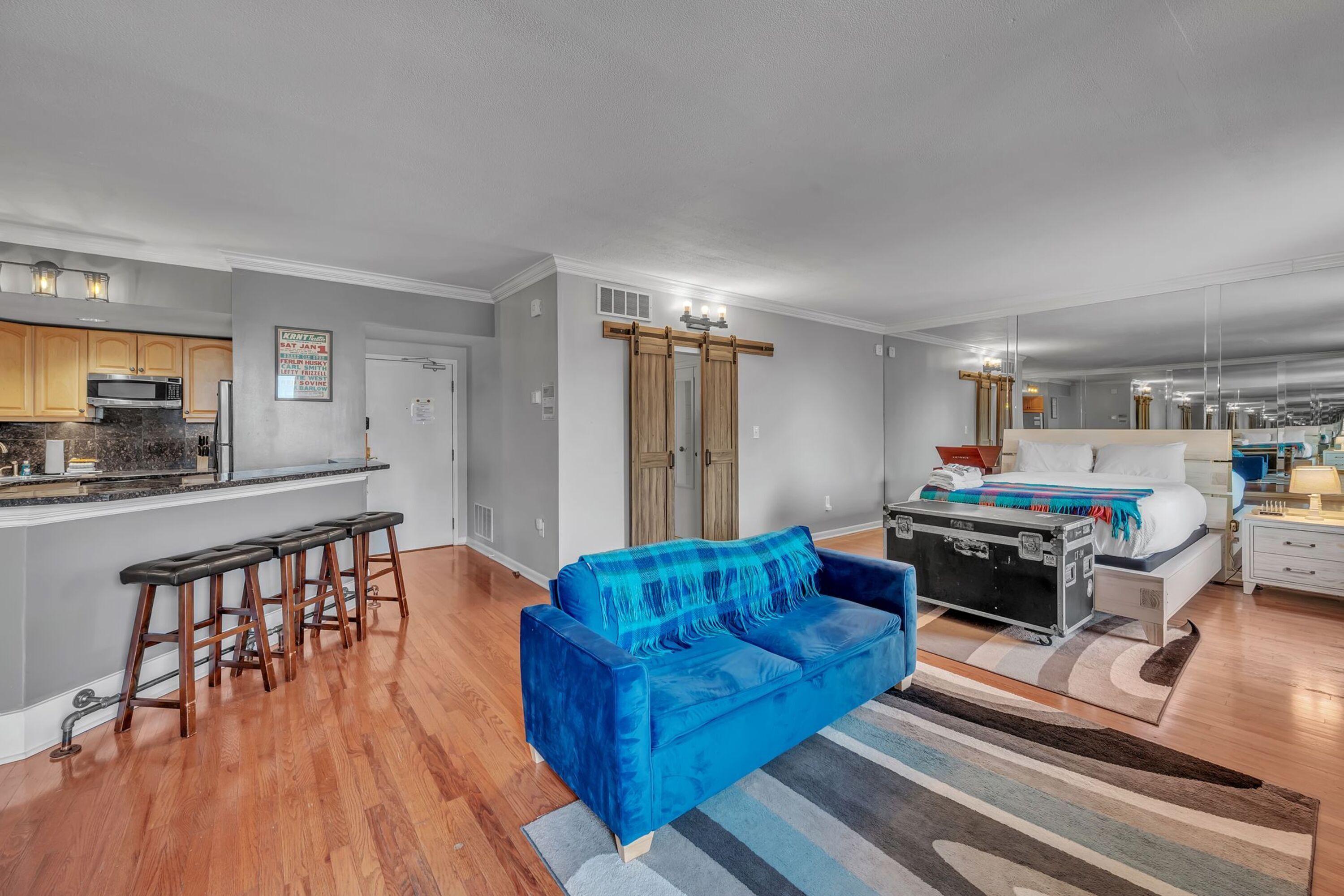A modern living space with a kitchen, a blue sofa, and a bed with a suitcase.
