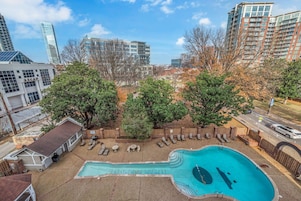 Zona residencial con piscina, árboles y edificios modernos al fondo.