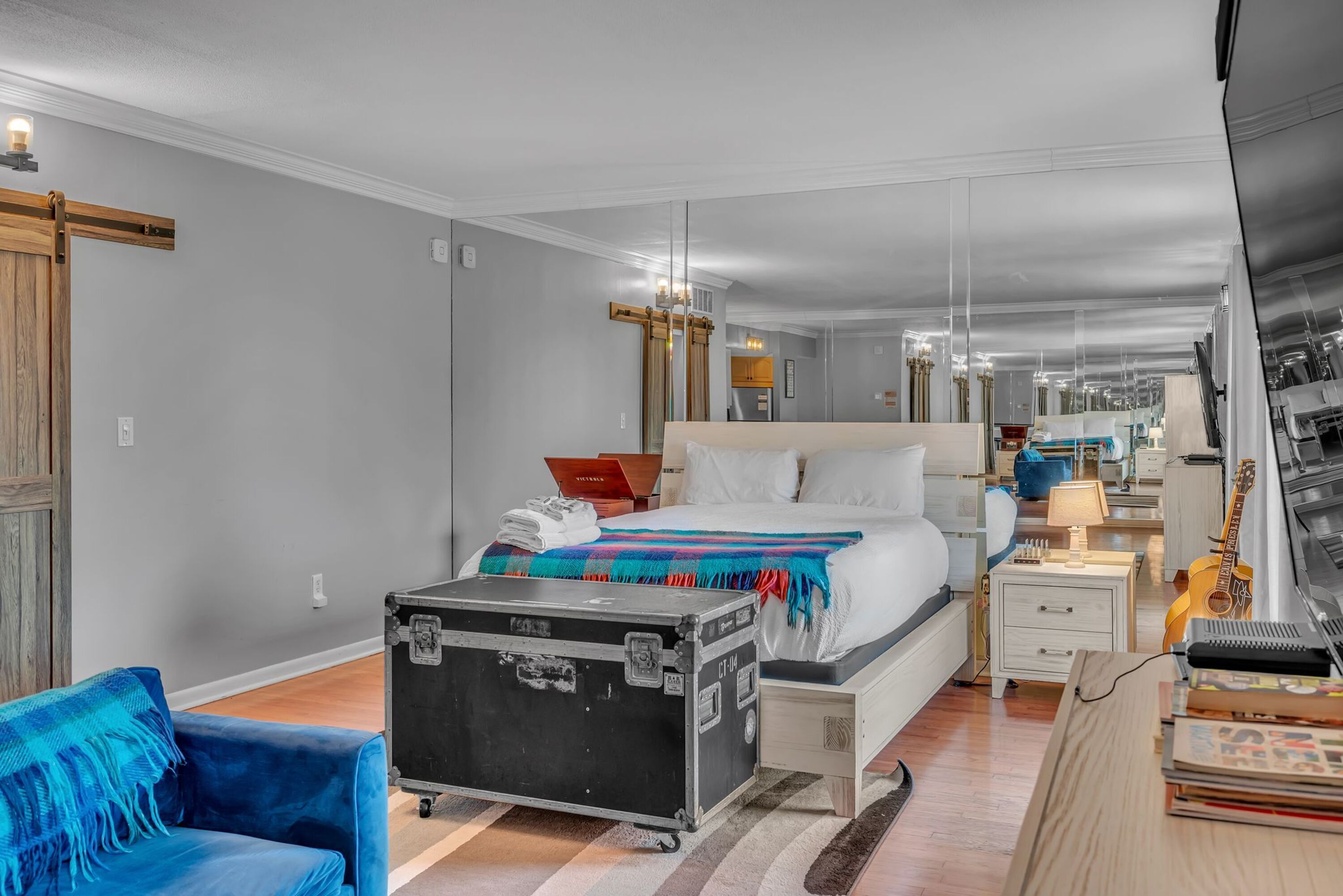 Une chambre d’hôtel moderne avec un lit, une valise, un bureau avec un ordinateur portable et une guitare.