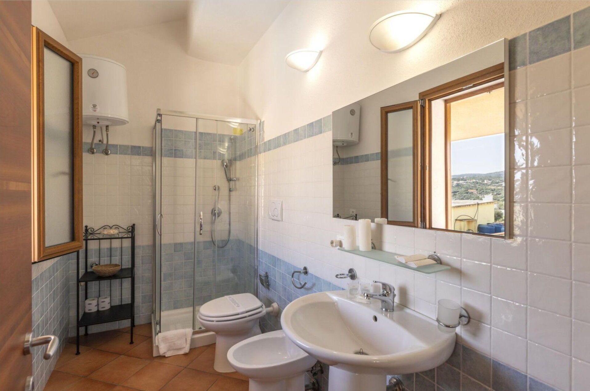Un bagno con doccia vetro, due servizi igienici, un lavandino e uno specchio.