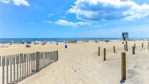 Ein Strand mit einer Holzzaun, Sonnenschirmen und einem Wegweiser.