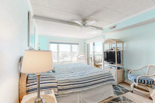 Un dormitorio con cama, televisor, una silla y balcón.