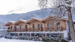Un chalet in legno con diversi balconi, ampie finestre e un paesaggio montano innevato.