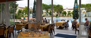 Un espace extérieur aménagé pour les repas, avec des tables et des chaises, une piscine en arrière-plan et des parasols.