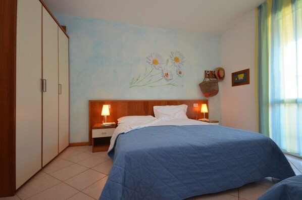 Une chambre à coucher avec un grand lit, deux tables de chevet avec des lampes, une armoire, un tableau au mur et une fenêtre avec des rideaux.